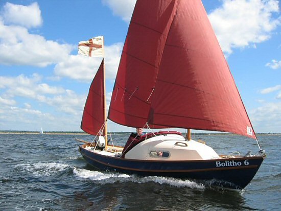 Een Coaster met donkerblauwe romp onder vol roodbruin zeil.