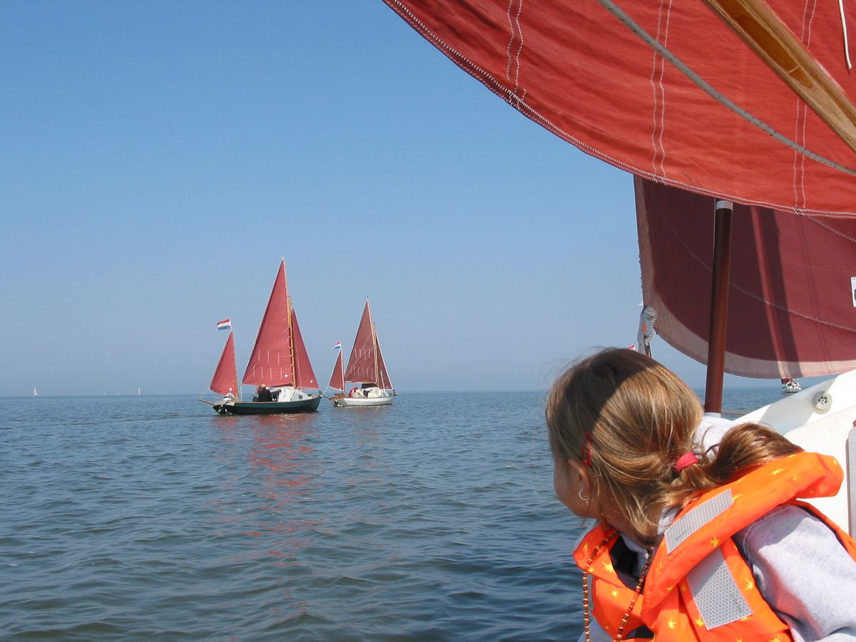 Uitzicht vanaf een Coaster onder zeil op twee andere Drascombes met roodbruine zeilen op open water.